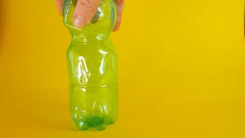A man's hand crushes a green disposable plastic bottle on a yellow background Stockbeeldmateriaal 103351525