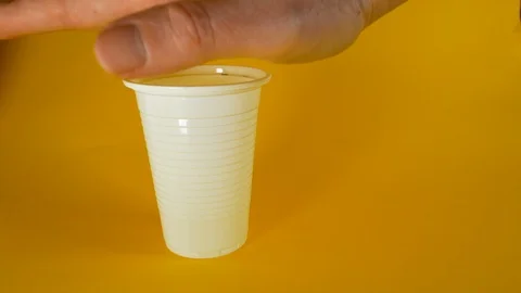 A man's hand crushes a white disposable plastic cup on a yellow background Stock Footage 103353370