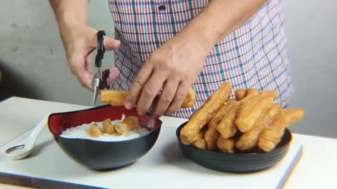 Man's hand cuts fried bread or cakwe using scissors over a bowl of porridge.. Video stock 338370480