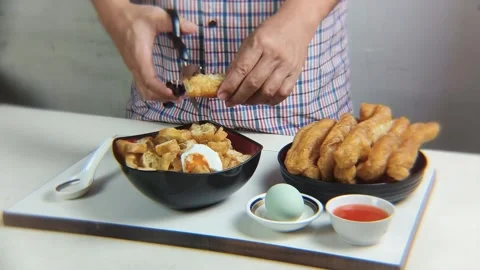 Man's hand cuts fried bread or cakwe using scissors over a bowl of porridge.. Video stock 338370540