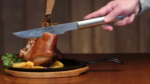 A man's hand cuts a large piece of meat from a pork knuckle with a knife. Ready 스톡 동영상 147311756
