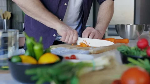Man's Hand Cutting Fresh Carrots On Chopping Board On Table with Vegetables Stock Footage 151327368