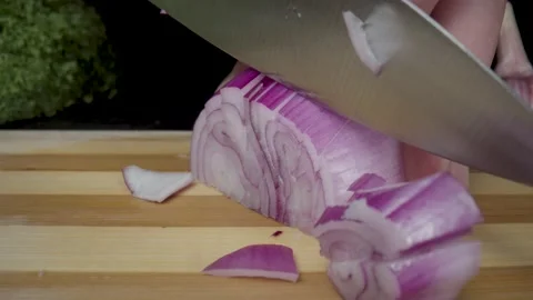 A mans hand cutting half an onion with a knife. Chopping an bulb on a wooden Stock Footage 203023346