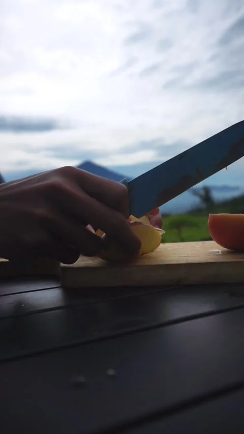 A man's hand is cutting a red apple on the table with a background of mountains Stock-Footage 300117826