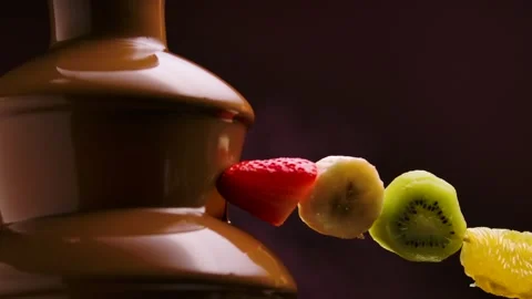 Man's hand dips a skewer with fruit in sweet melted chocolate in chocolate Stock Footage 148355473
