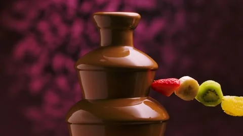Man's hand dips a skewer with fruit in sweet melted chocolate in chocolate Stock Footage 148356719
