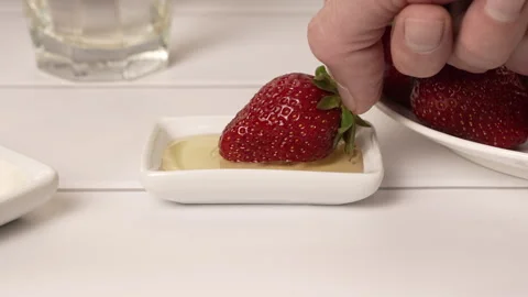 A man's hand dips strawberries in liquid honey Stock Footage 243377368