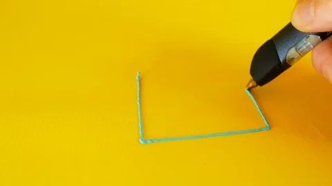 A man's hand draws a small house on a yellow background with a 3D printer pen Video stock 103374359