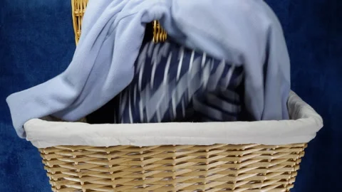 A man’s hand dropping clothes to be washed into a wicker laundry basket. Stock Footage 301057368