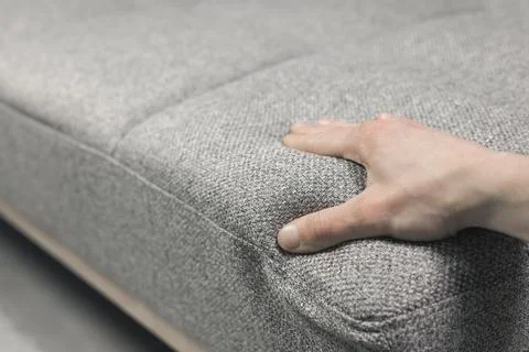 A man's hand feels the softness of a modern grey fabric sofa. Home or offic.. Stock Photos