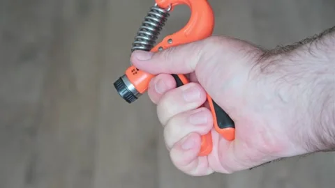 Man's hand forcefully squeezes orange-colored power trainer with metal spring fo Stockbeeldmateriaal 247177335