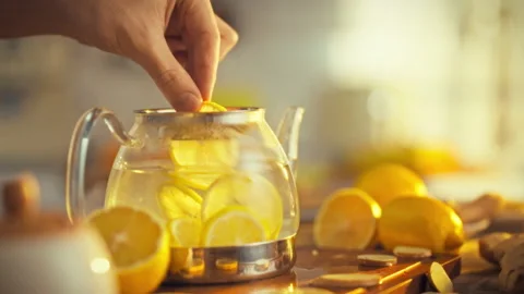 Mans hand gently places fresh lemon slice into teapot releasing zest into ho Stock Footage 331355151