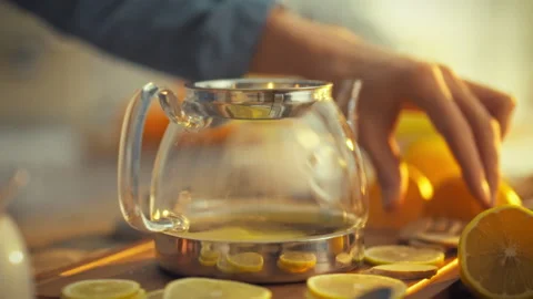 Mans hand gently places a fresh slice of citrus into a teapot releasing a dr Stock Footage 331473400