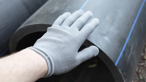 A man's hand in a gray work glove slaps a large diameter black plastic pipe Stock Footage 286027880