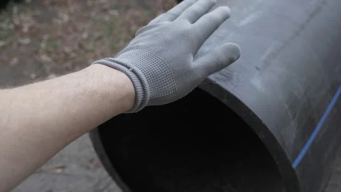 A man's hand in a gray work glove slaps a large diameter black plastic pipe. Stock Footage 288436842