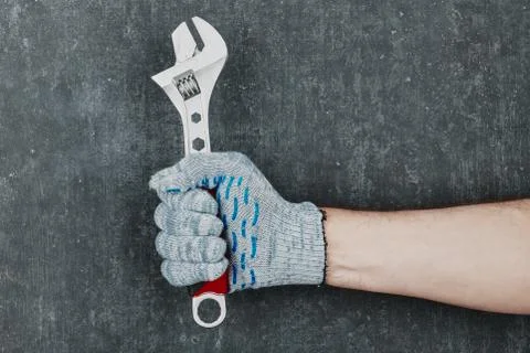 Man's hand holding an adjustable spanner wrench on gray background, man's han Stock Photos