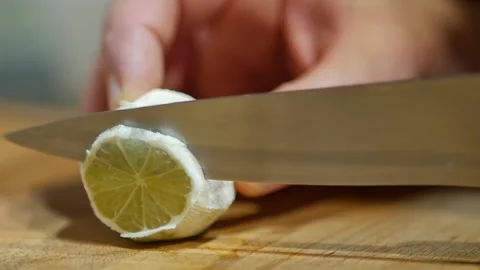 Man's hand holding half of a sliced lemon on a wooden chopping board with a Stock Footage 143793553