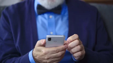 Man's hand holding the phone, the camera rises up to the face of the elderly man Video stock 235943374