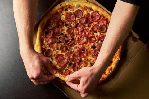 Man's hand is holding slice of double cheese pizza from whole Pizza in a card Stock Photos
