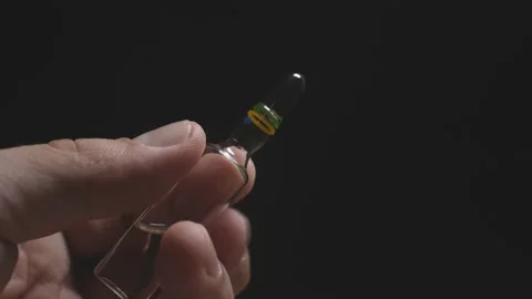 Man's hand holds an ampoule for injection on a dark background. coronavirus Stock Footage 127754271