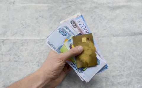 A man's hand holds a bundle of Russian rubles and plastic cards Stock Photos