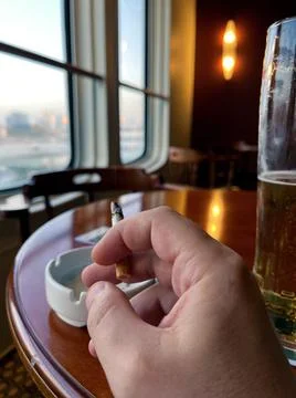 A man's hand holds a cigarette against the background of windows in a beer bar Stock Photos