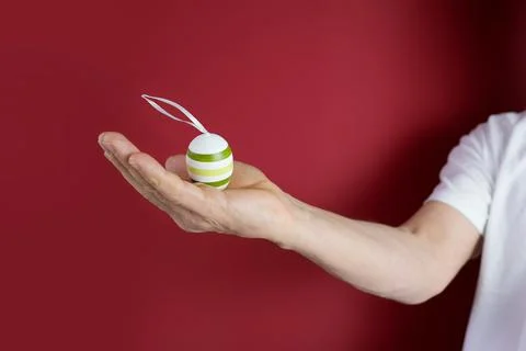 Man's hand holds a colored Easter egg with a drawn pattern, red background, c Stock Photos