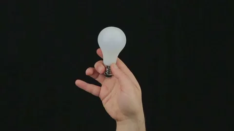 Man's hand holds a light bulb that lights up Stock Footage 185490073