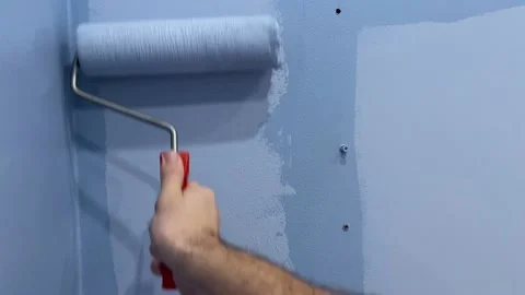A man's hand holds a roller brush and paints the wall in lilac color Stock Footage 216843032