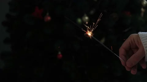 A man's hand holds sparkler on the background of Christmas tree with garland. 4K Stock Footage 167316865