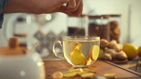 A mans hand infuses steaming tea with a fresh ginger slice in a cozy kitchen Stock Footage 331309583