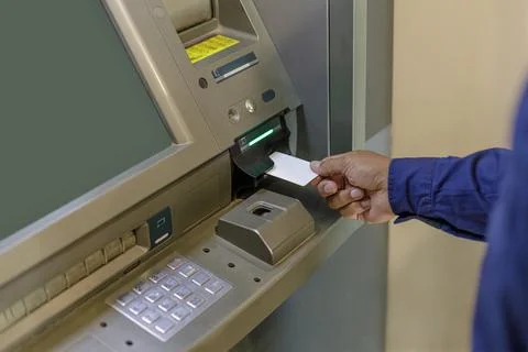 A man's hand inserting a blank card into an ATM. 스톡 사진