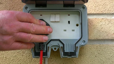 Mans hand inserting a British plug into a socket on an outside brick wall. Stock Footage 157044540