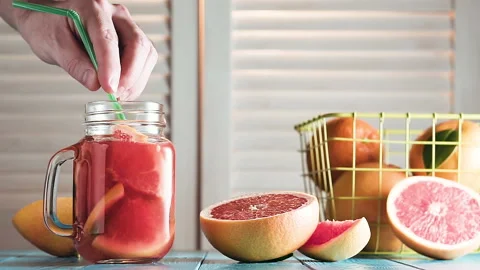 Man's hand is inserting drinking straw into the cocktail of grapefruit juice. Stock Footage 87348872