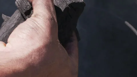 Man's hand inserting pieces of charcoal into a barrel for roasting Stock Footage 154214848