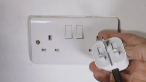 Man’s hand inserting UK British travel plug into wall socket and switching on. Vídeos de archivo 281083092