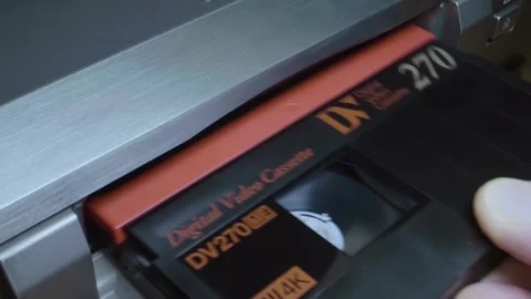 A man's hand inserts a cassette into a silver-colored DV tape recorder Stock Footage 297814658