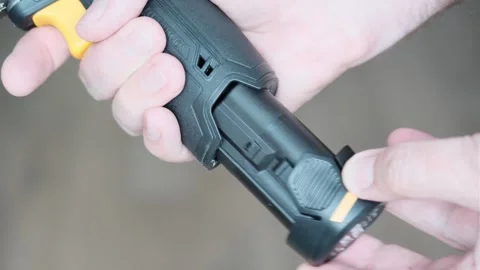 Man's hand inserts charged battery into drill to drill on gray background. Close Stock Footage 247498797