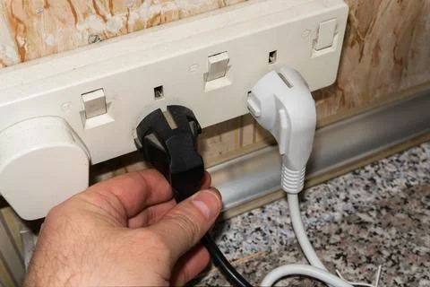 A man's hand inserts a plug into a socket. Sockets in the wall, wires in the Stock Photos