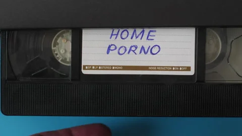 A man's hand inserts a video cassette with the inscription home porn into a.. Stock Footage 233962514