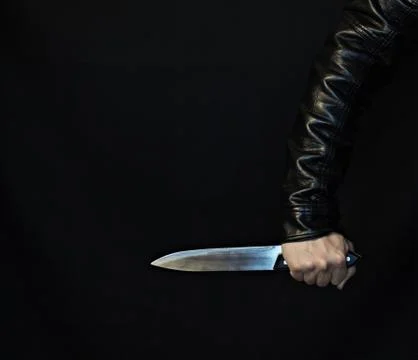 A man's hand in a jacket with a knife on a black background Stockfoto's