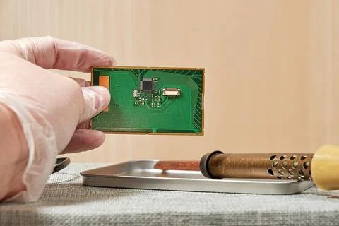Man's hand keeps a PCB with a chip in the laboratory above the table Stock Photos