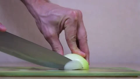 A man's hand with a knife cuts half an onion on the table. Macro shot. Video stock 155888474