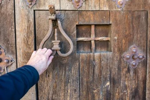 Man's hand knocking with a knocker on an ancient wooden door in the medieval Stock Photos