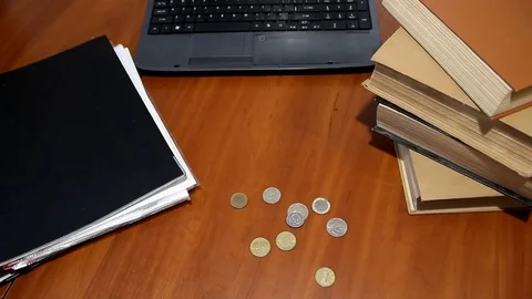 A man's hand is laying coins on a table next to books and a laptop, the top view Video stock 83247109