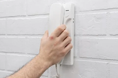 A man's hand lifts a white intercom telephone Stock Photos