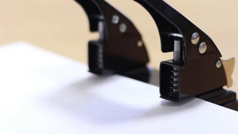 Man's hand makes holes in sheet of paper with a hole punch. Stockbeeldmateriaal 141843183