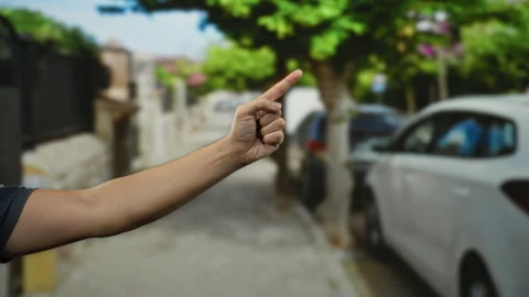 Man's hand making thumbs up and pointing gestures in a city street with par.. Video stock 306854057
