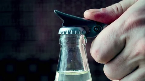 A man's hand opens a bottle of mineral water with a bottle opener in an indoor Stock Footage 164064758