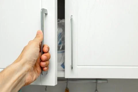 A man's hand opens a kitchen cabinet door Stock Photos